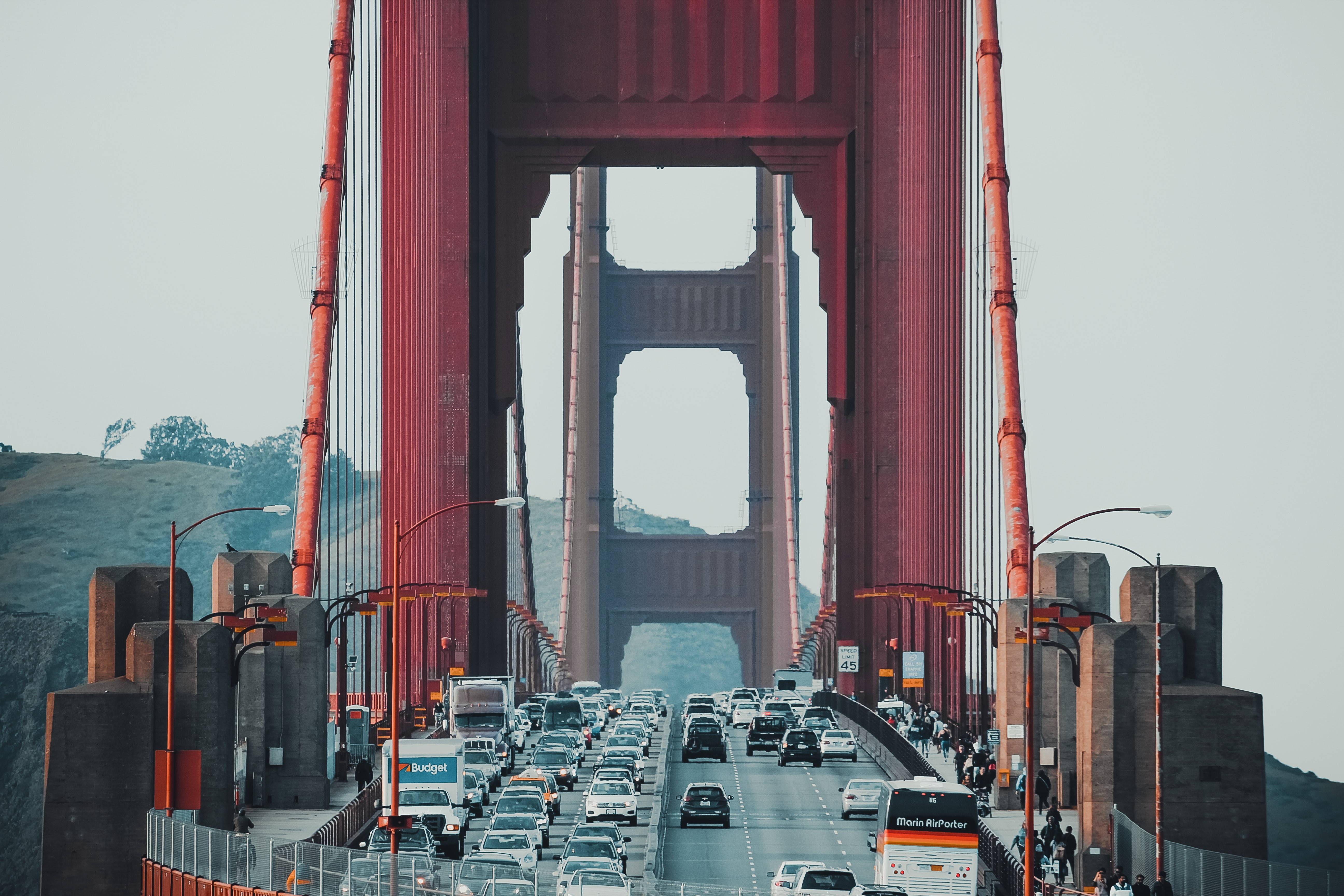 Traffic crossing the Golden Gate Bridge in San Francisco, including cars, trucks, and a coach on the highway with pedestrians and bicyclists on the pathways.